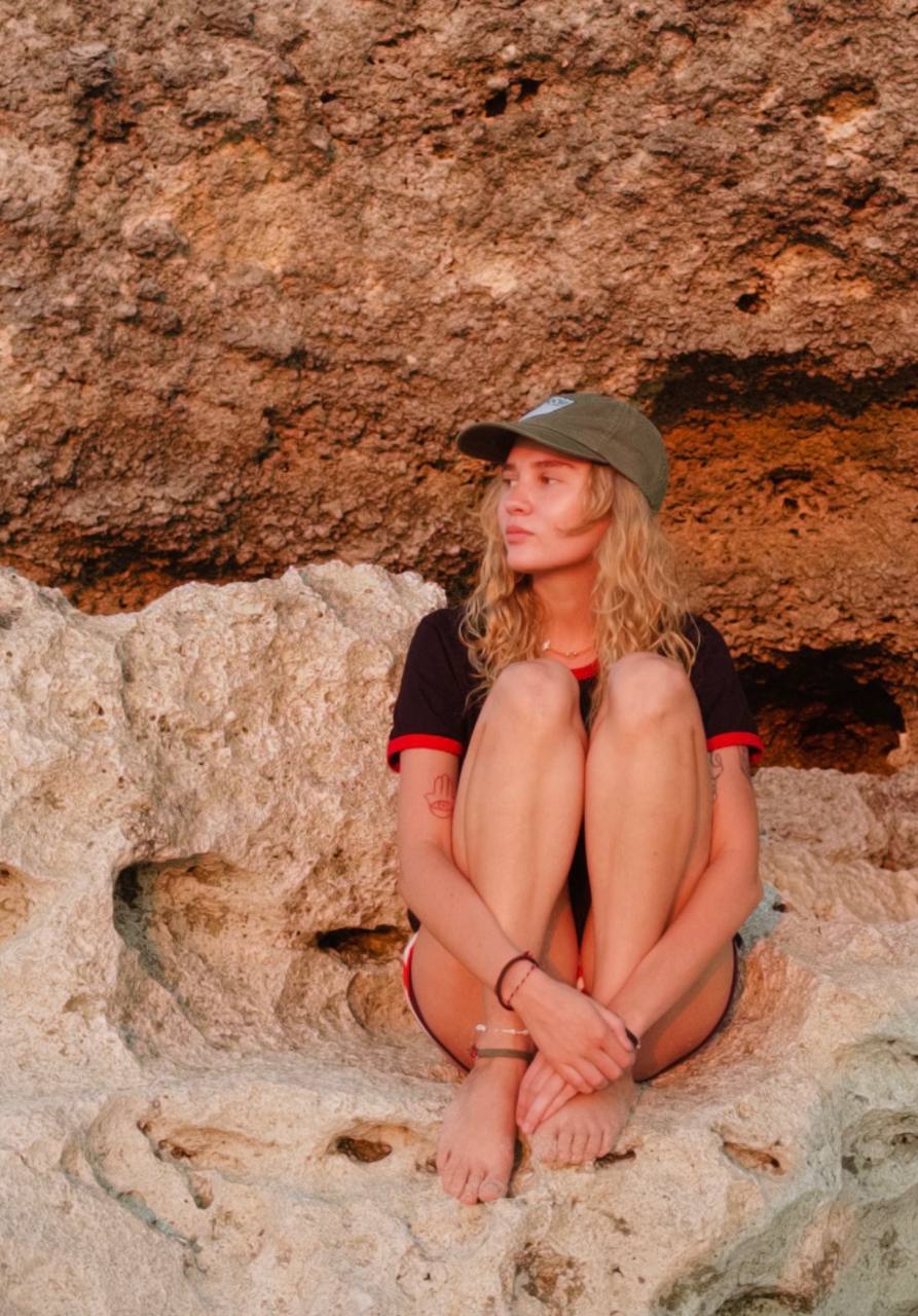 Woman sitting cross-legged on a light-colored rock formation, wearing a cap