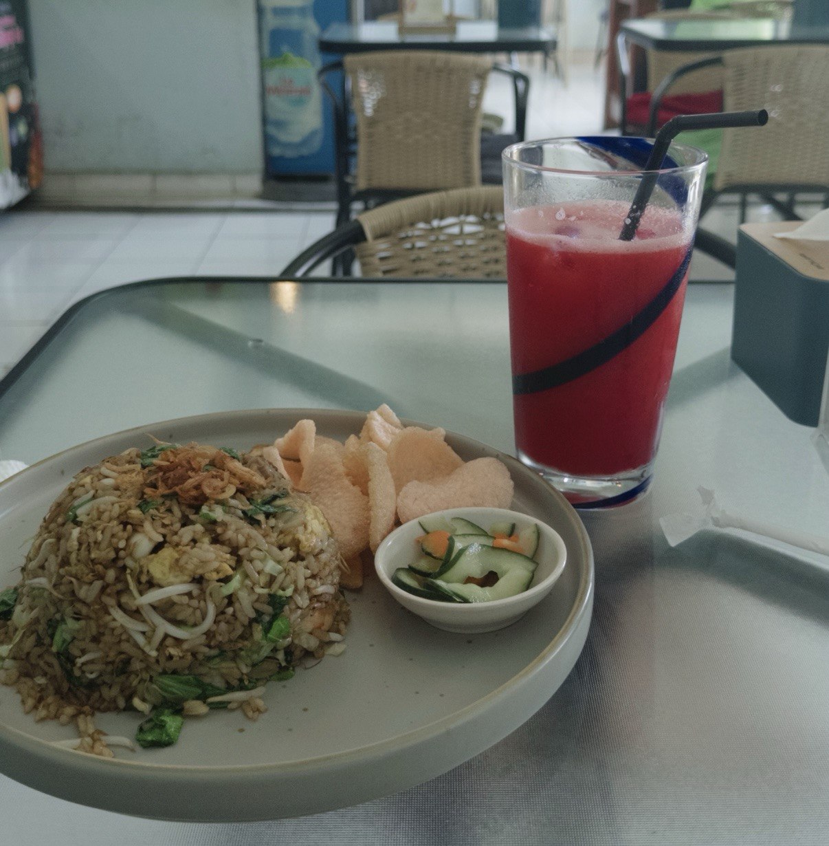Plate of fried rice with sides and a red iced drink on a café table