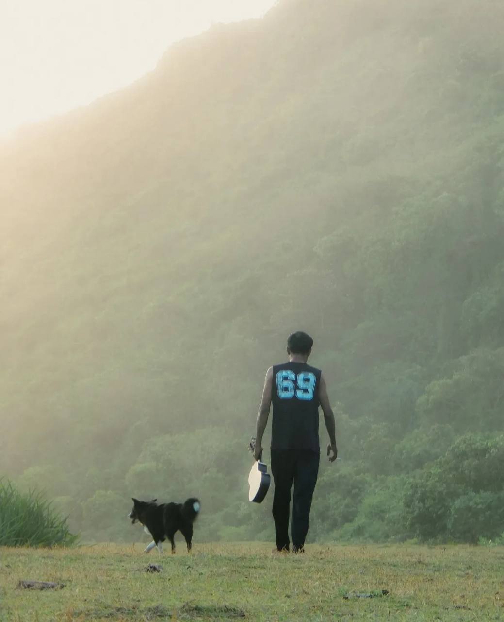 Silhouette of a man with a dog walking through misty hills at sunset