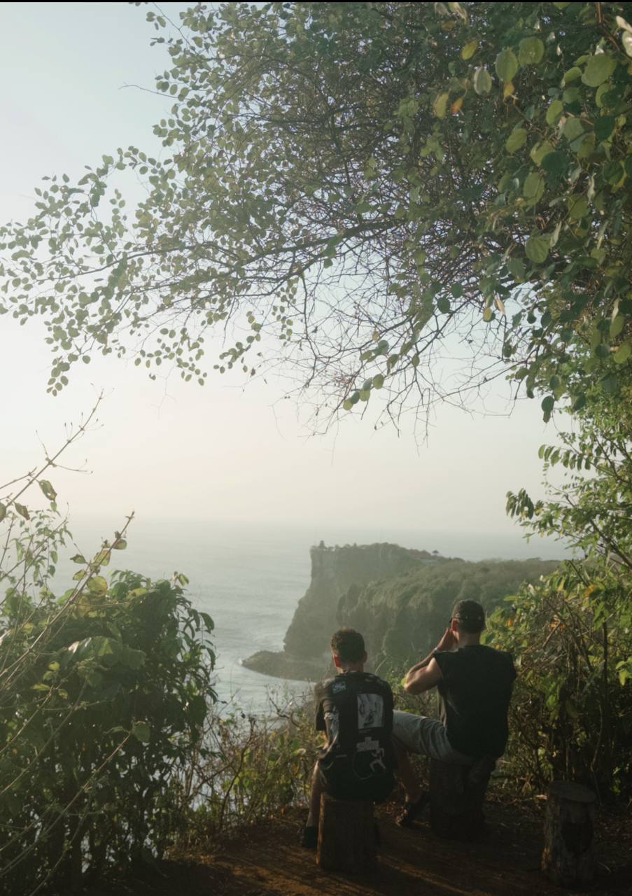 Two friends sitting on tree stumps overlooking the Uluwatu cliffs and ocean