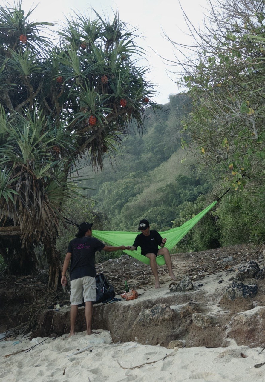 Two people at a jungle clearing near the beach, green hammock strung between trees