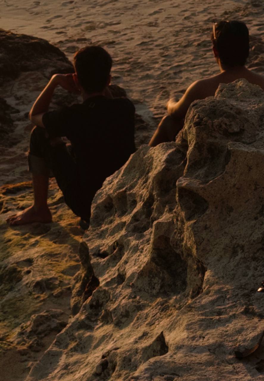 Two people sitting on rocks at the beach, golden sunset light