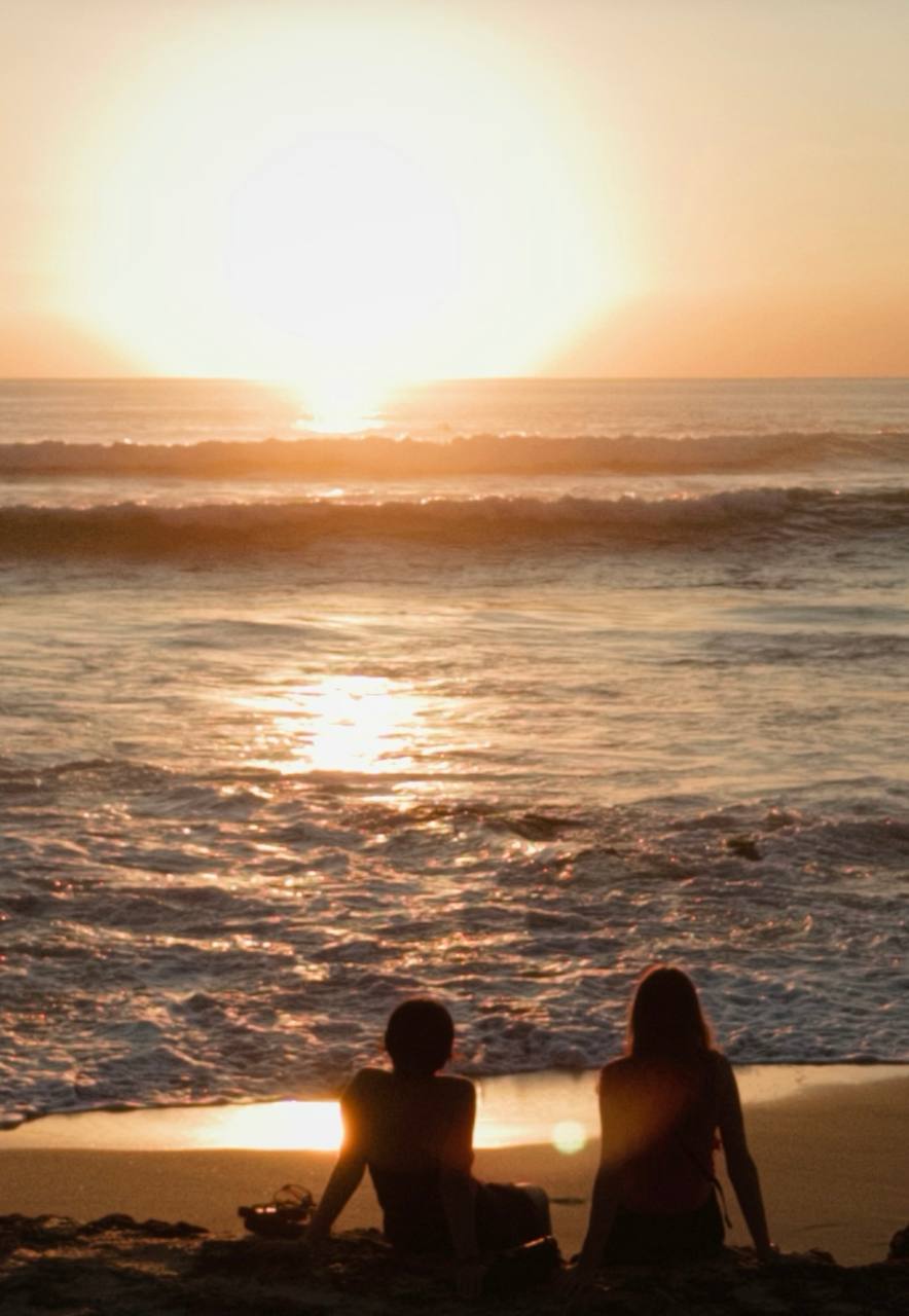 Two people sitting on the sand watching the sunset over the ocean